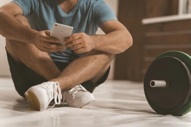 Man using free workout apps on his phone while resting after a strength training session.
