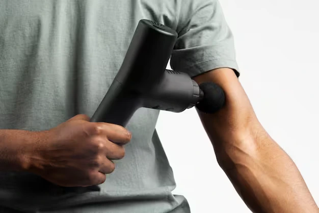 Person using a percussion massage gun as part of muscle recovery devices.