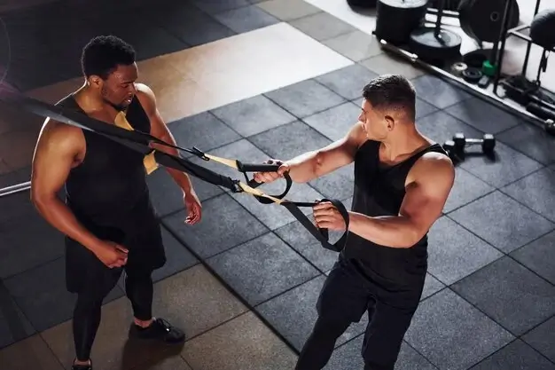 Two men training in a gym using resistance bands vs weights for functional strength.
