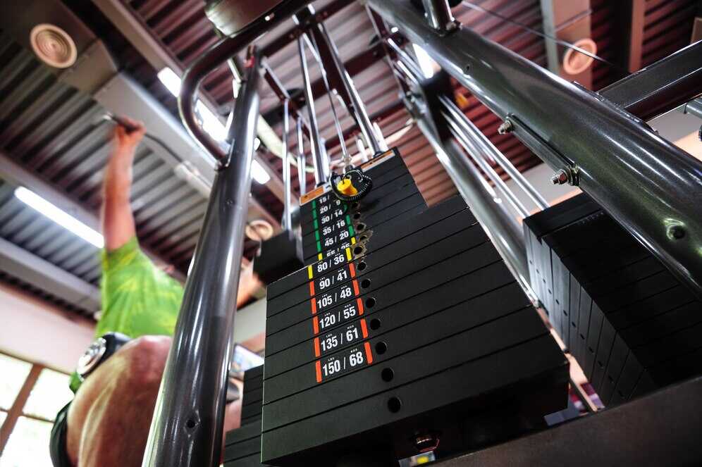 A beginner uses a lat pulldown machine with adjustable stack weights, showing weight machines for beginners in action.