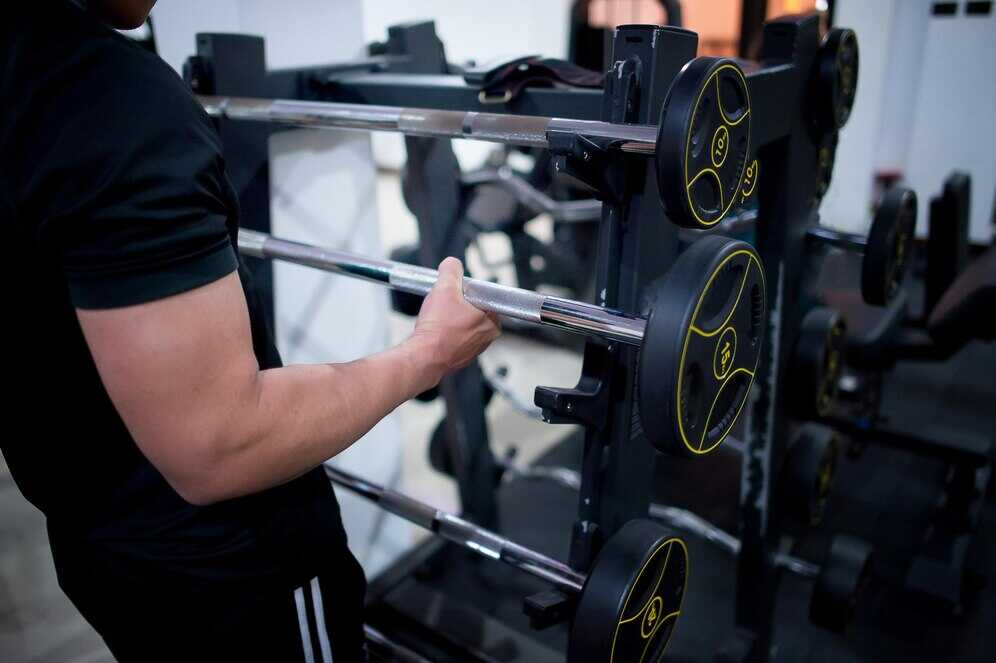 A gym-goer holds a barbell in a weight area, highlighting the difference between free weights and weight machines for beginners.