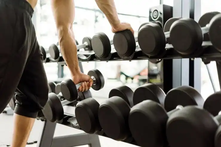 A man selecting a dumbbell from a gym rack before starting a dumbbell workout session.