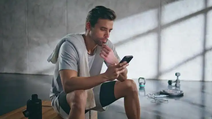 A man reviewing his fitness app after a dumbbell workout in a minimalist home gym setting.