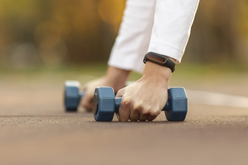 A person gripping blue dumbbells outdoors as part of a focused dumbbell workout routine.
